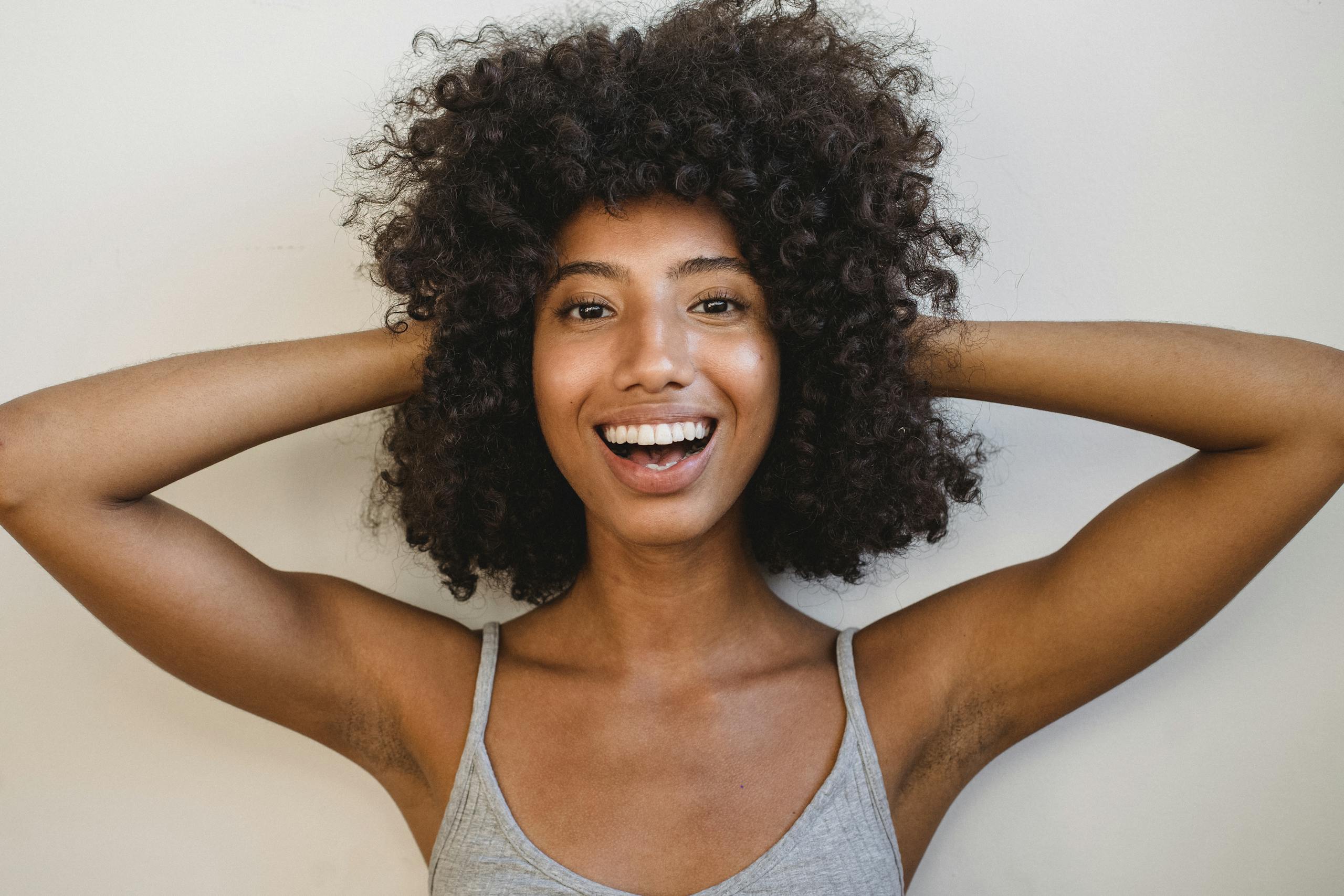 Delighted black woman touching hair and looking at camera